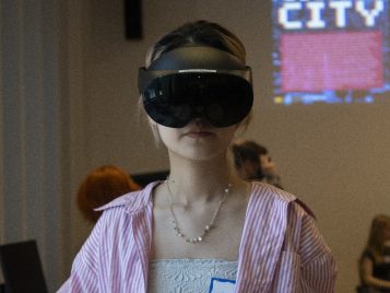 Naomi Zheng stands with a black virtual reality headset, holding a paper that lists her name and project title.